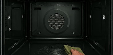 Hand veegt met een doek de bodem van een lege ovenruimte schoon