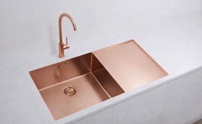 Rosé gouden dubbele spoelbak met bijpassende kraan in een wit keukeneiland met strak werkblad
