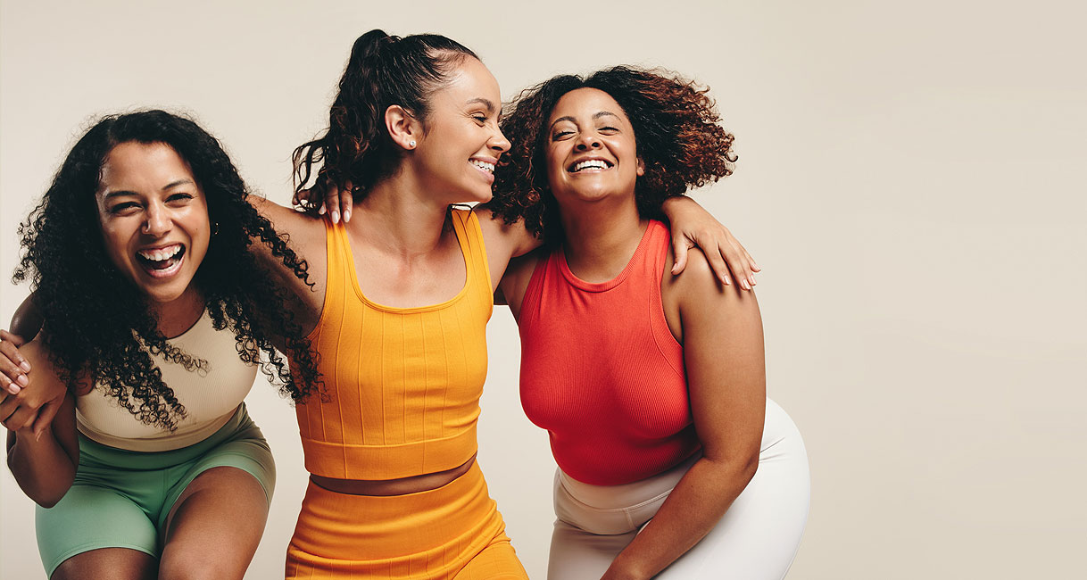 Drie lachende vrouwen in kleurrijke sportkleding na het sporten voor het downloadbare sportkleding wasprogramma
