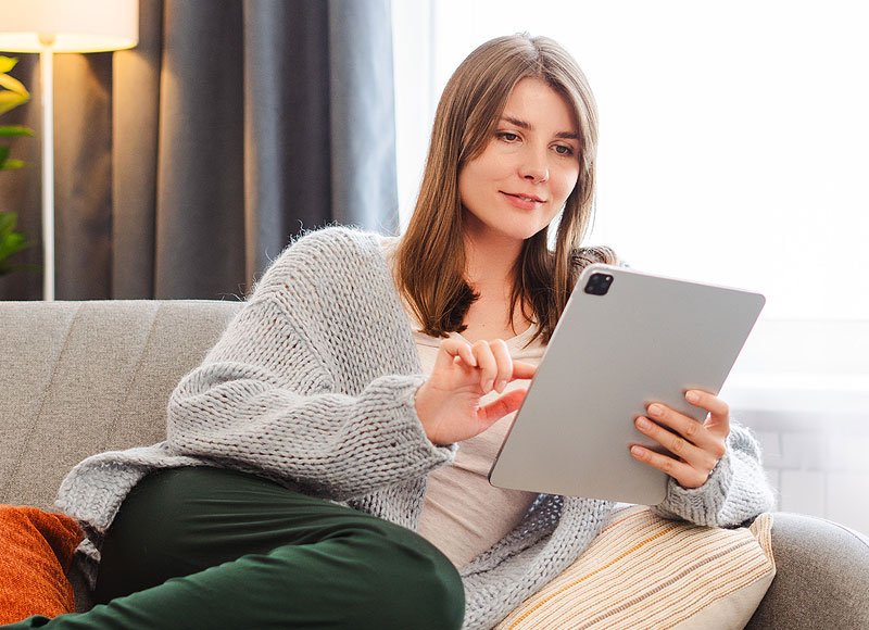 Vrouw bekijkt keukeninspiratie op tablet vanaf de bank in een lichte woonkamer