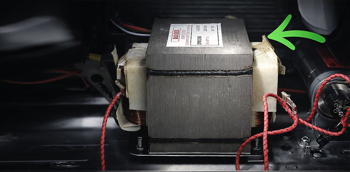 Transformator binnenin magnetron met groene pijl die de spanningsopvoering van 230 naar 4000 volt aanwijst