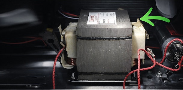 Transformator binnenin magnetron met groene pijl die de spanningsopvoering van 230 naar 4000 volt aanwijst