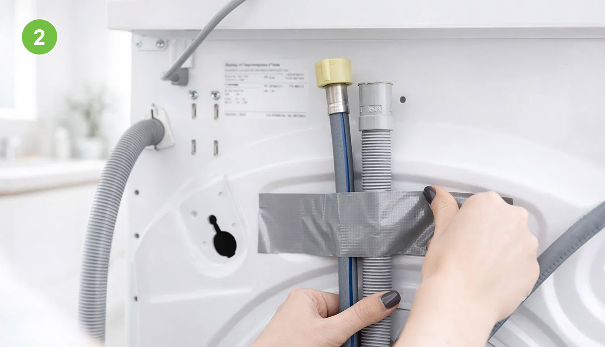 Handen tapen de afvoer- en toevoerslang met ducttape vast aan de achterkant van een wasmachine