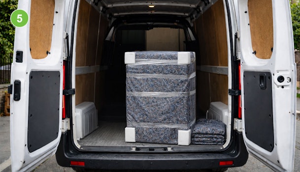 Ingepakte wasmachine rechtopstaand in verhuisbus, omwikkeld met verhuisdeken en krimpfolie