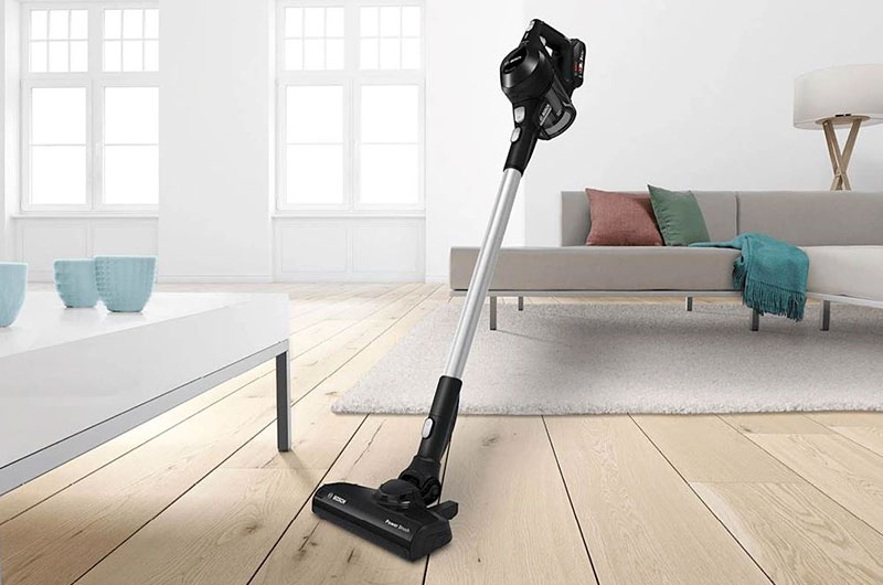 Zwarte steelstofzuiger met accu staat op houten vloer in moderne woonkamer met bank