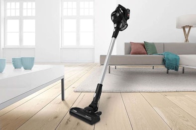 Zwarte steelstofzuiger met accu staat op houten vloer in moderne woonkamer met bank