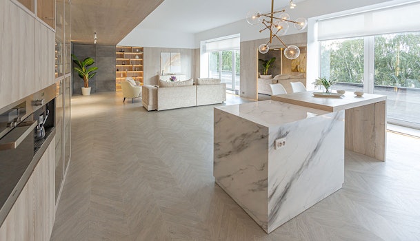 Grote moderne woonkamer met open keuken en marmeren kookeiland op houten vloer toont ruim oppervlak