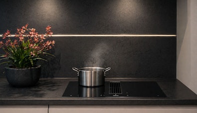 Pan met opstijgende stoom op kookplaat met geïntegreerde afzuiging in donkere keuken