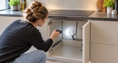 Vrouw schijnt met een zaklamp op het stopcontact in de keukenkast onder de kookplaat