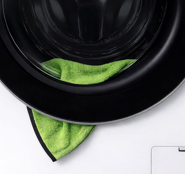 Close-up van wasmachinedeur met groene handdoek die tussen de deur en manchet klemt