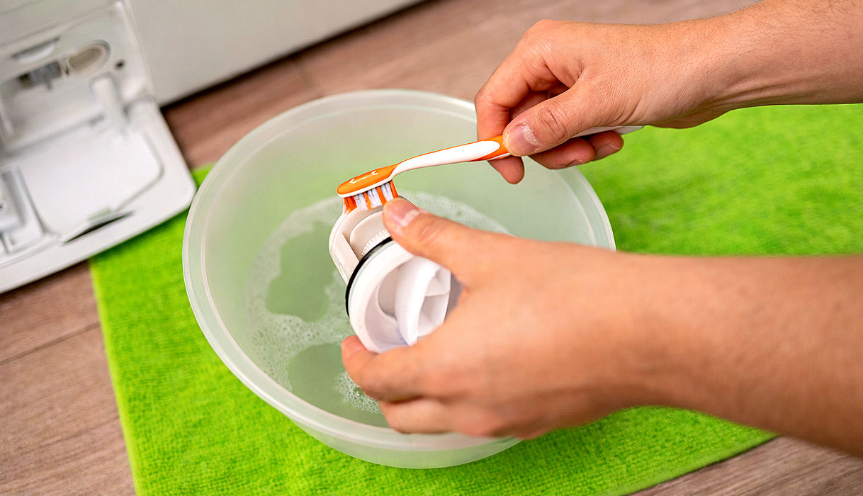 Hand reinigt het pompfilter van een LG wasmachine boven een opvangbak met water
