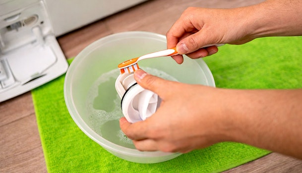 Hand reinigt het pompfilter van een LG wasmachine boven een opvangbak met water