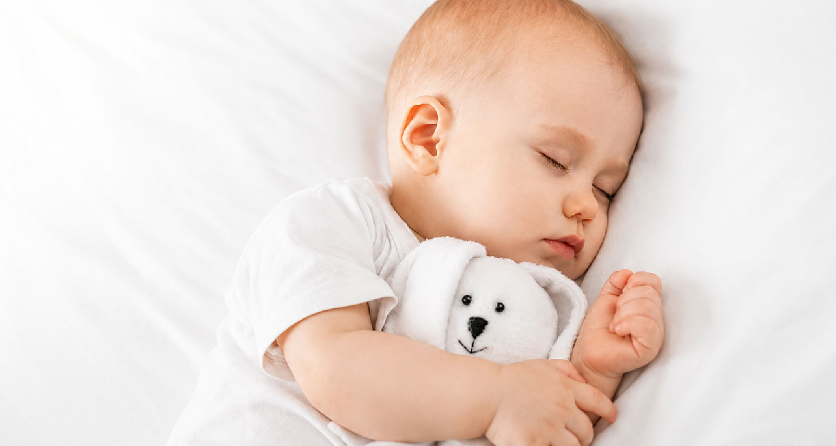 Slapende baby met knuffel naast een supersilent Pelgrim vaatwasser van 41 dB