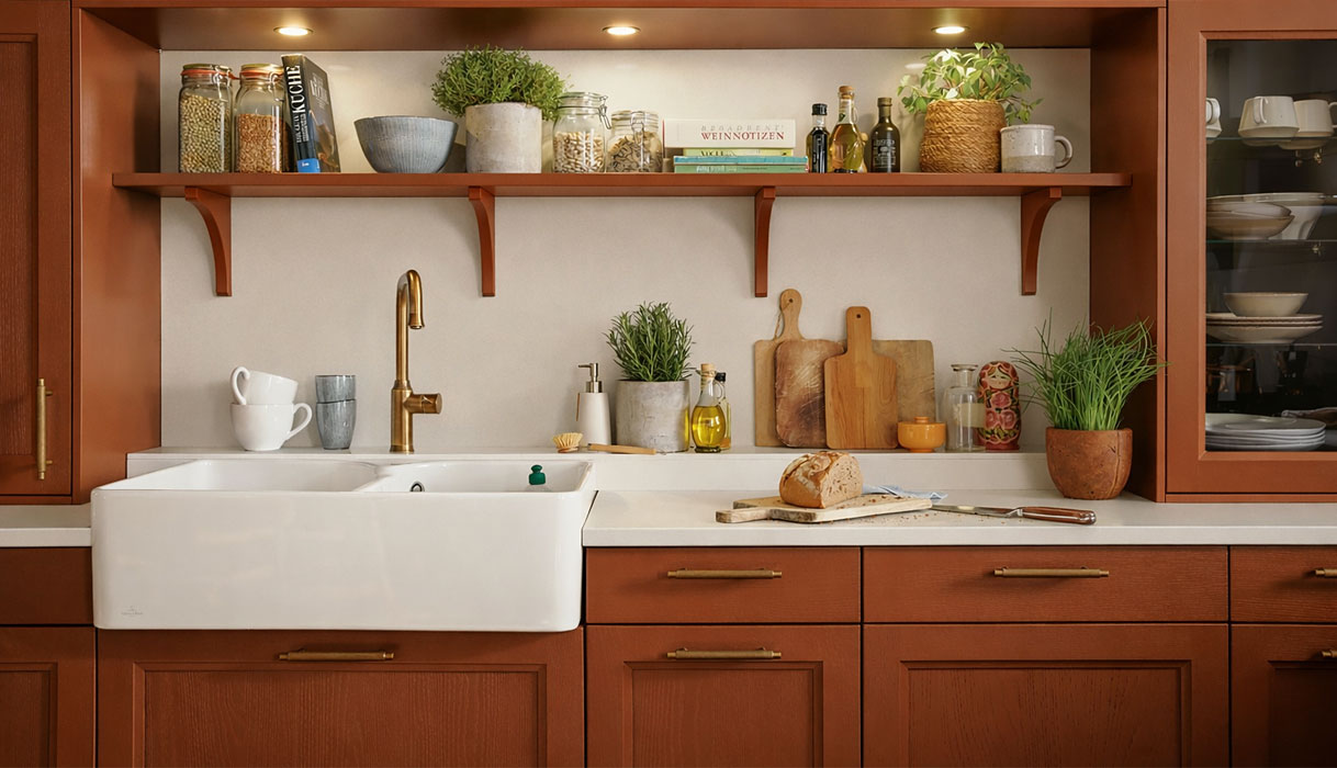 Terracotta keuken met klassieke fronten, witte spoelbak en open plank met kruiden en keukengerei.