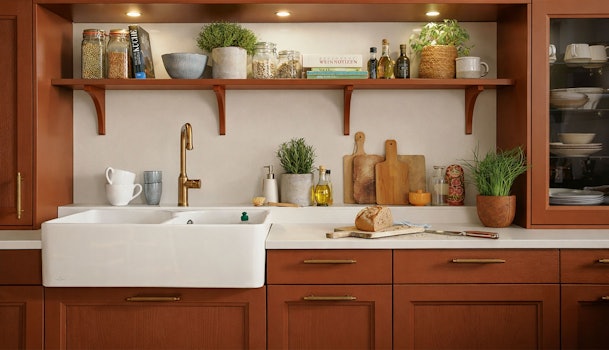 Terracotta keuken met klassieke fronten, witte spoelbak en open plank met kruiden en keukengerei.