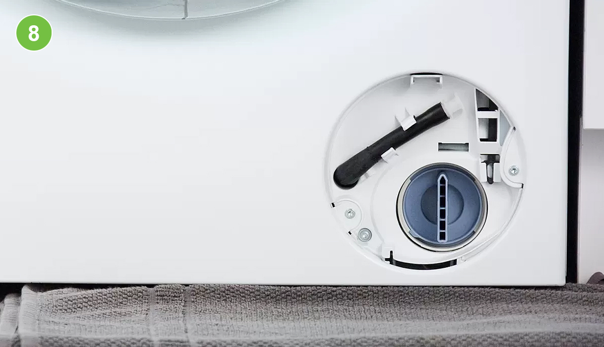 Pompfilter teruggeplaatst in het filtercompartiment van een wasmachine, de noodafvoerslang is teruggehangen in de houder