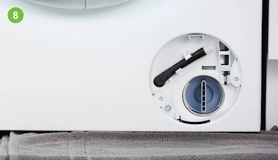 Pompfilter teruggeplaatst in het filtercompartiment van een wasmachine, de noodafvoerslang is teruggehangen in de houder