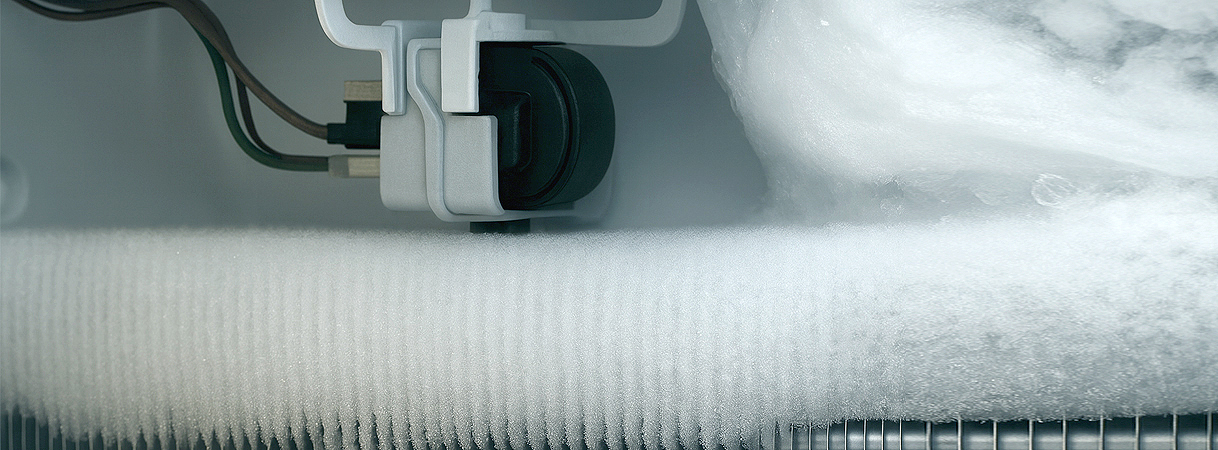 Ijsvorming rond onderdelen in een koelkast, met zichtbare leidingen en mechaniek.