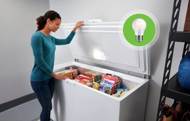 Vrouw bekijkt ingevroren producten in een goed geplaatste vrieskist in de schuur, met verlichting en ruimte rondom voor ventilatie.