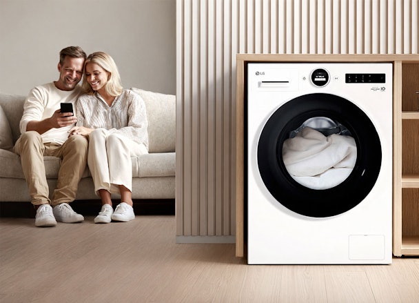 Vrouw bedient LG wasmachine op afstand via smartphone met ThinQ app in moderne woonkamer