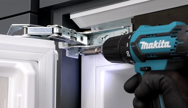 Monteur bevestigt het scharniermechanisme van een inbouwkoelkast met een accuschroefmachine