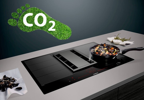 Inductiekookplaat met geïntegreerde afzuiging waarop een pan staat te koken, met een CO₂-voetafdruk als symbool voor lagere uitstoot bij inductie.