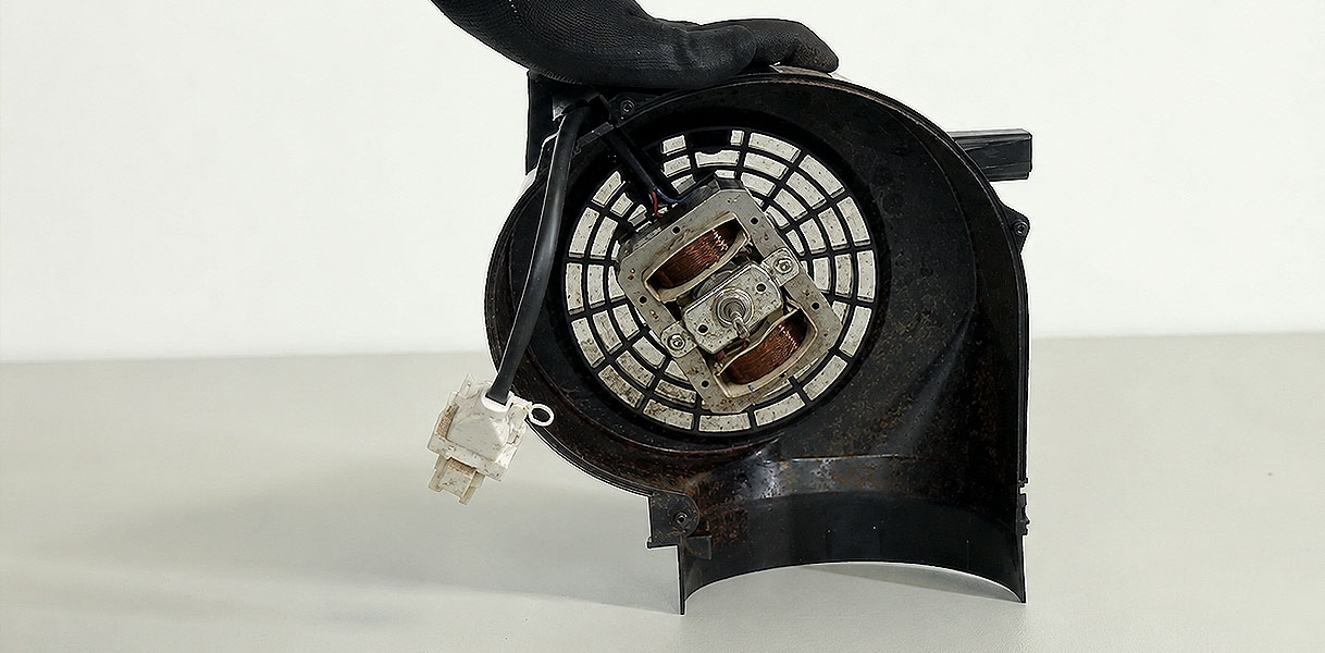 Hand met handschoen houdt een versleten motor met ventilatorwiel van een afzuigkap vast