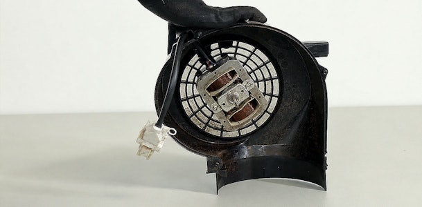 Hand met handschoen houdt een versleten motor met ventilatorwiel van een afzuigkap vast