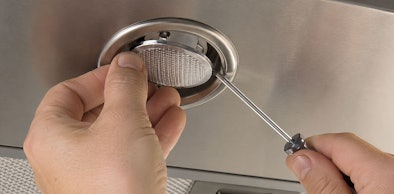 Handen wippen met een schroevendraaier het afdekglaasje van een lampje los in een Siemens afzuigkap