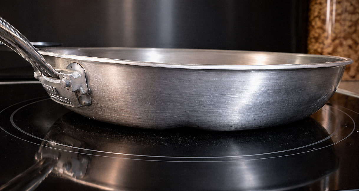 RVS pan op inductiekookplaat gezien van opzij om de vlakheid van de bodem te beoordelen