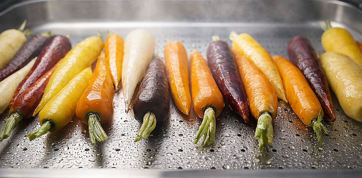 Kleurrijke wortels die worden gestoomd in een stoommandje voor gezonder koken met behoud van vitamines