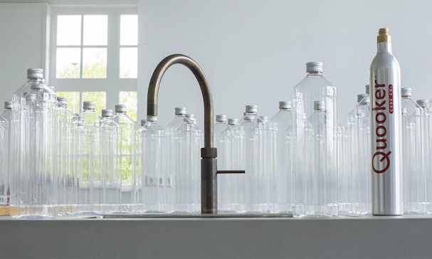 Quooker 5-in-1 kraan met CUBE tussen lege waterflessen en CO2-cilinder als alternatief voor flessenwater