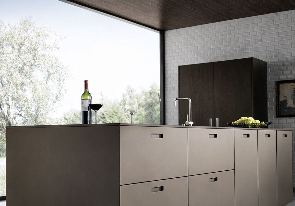 Modern donker keukeneiland met ingebouwde spoelbak, wijnglazen en een kom fruit voor een groot raam met tuinuitzicht