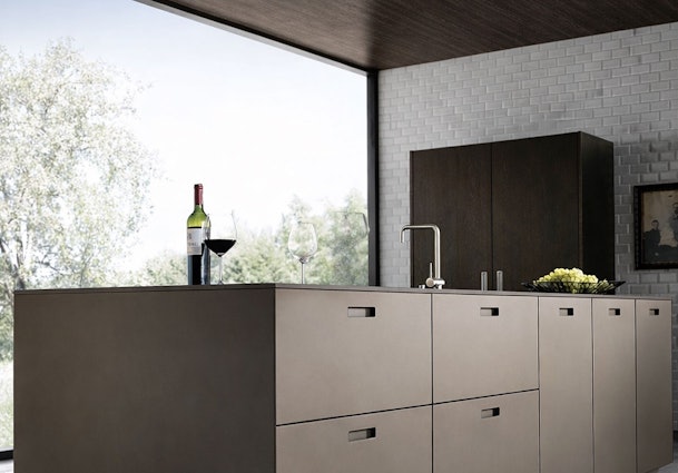 Modern donker keukeneiland met ingebouwde spoelbak, wijnglazen en een kom fruit voor een groot raam met tuinuitzicht