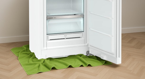 Onderzijde van een openstaande vriezer met groene handdoeken rondom geplaatst om smeltwater op te vangen.