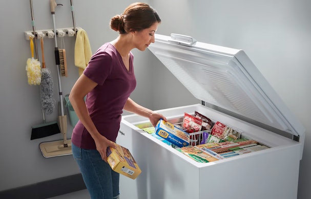 Vrouw die diepvriesproducten opbergt in een vrieskist in de schuur