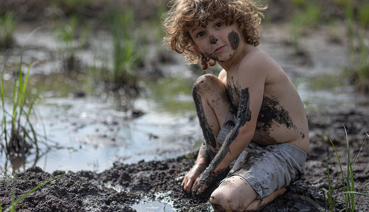 Kind speelt in de modder met vieze kleding