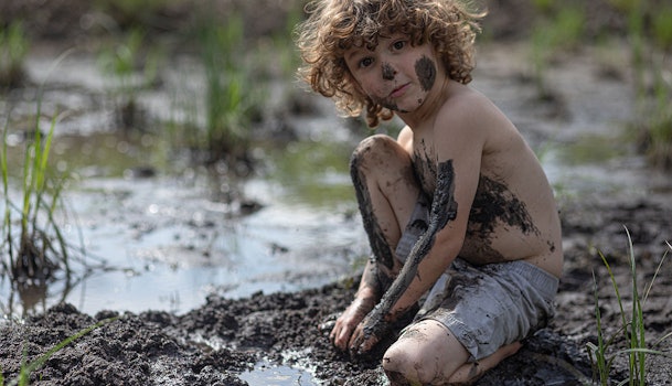 Kind speelt in de modder met vieze kleding