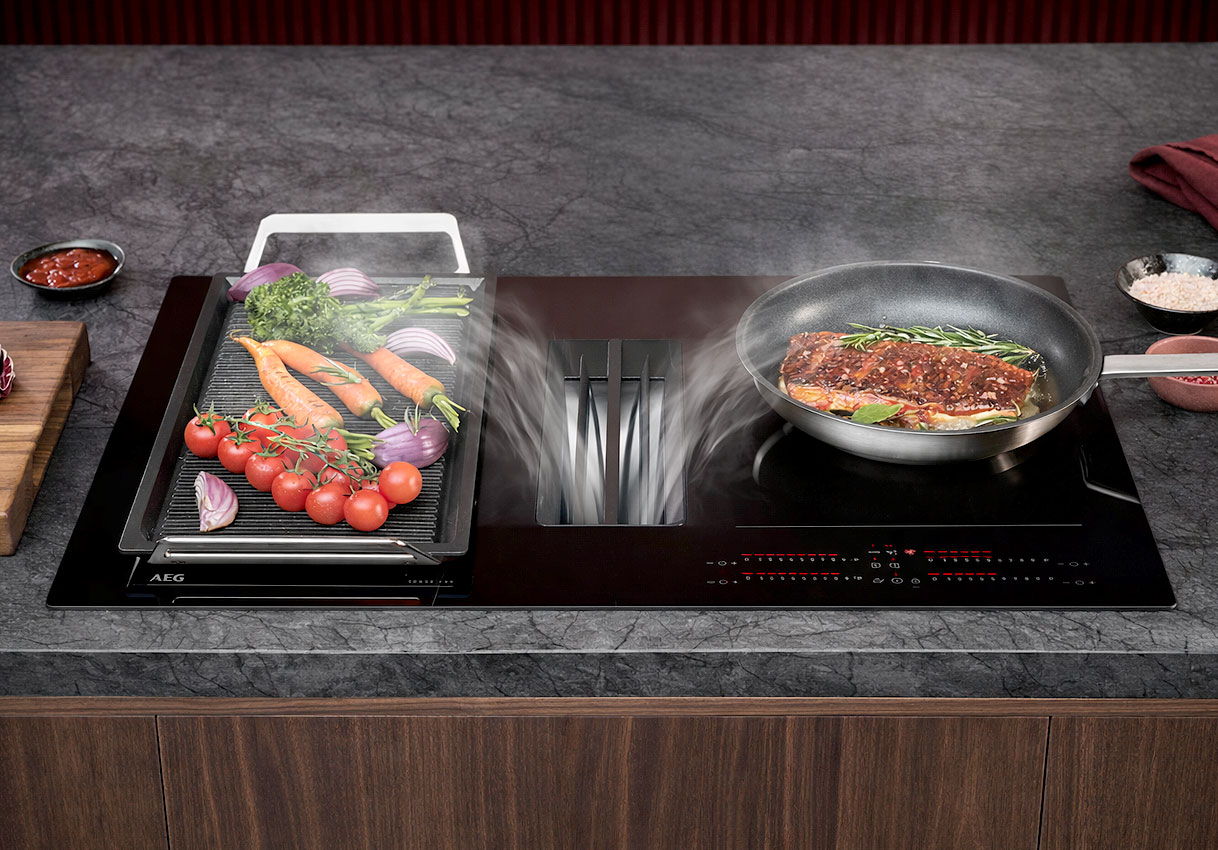 AEG inductiekookplaat met geïntegreerde afzuiging en pannen met groenten op het kookoppervlak