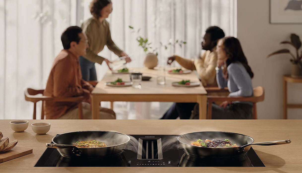 Miele inductiekookplaat met geïntegreerde afzuiging in een open keuken met gezin op de achtergrond