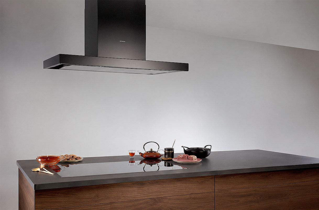 Strakke wandschouw afzuigkap boven een keukenblad met theeservies en wok in een moderne keuken