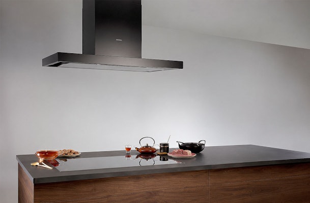 Strakke wandschouw afzuigkap boven een keukenblad met theeservies en wok in een moderne keuken