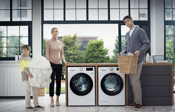 Gezin met kind naast LG wasmachine en droger in moderne wasruimte met wasmand