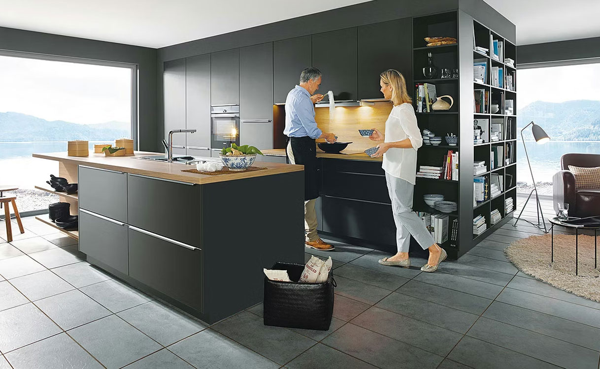 Een woonkeuken met een donker spoeleiland en een aangrenzende woonkamer met grote ramen
