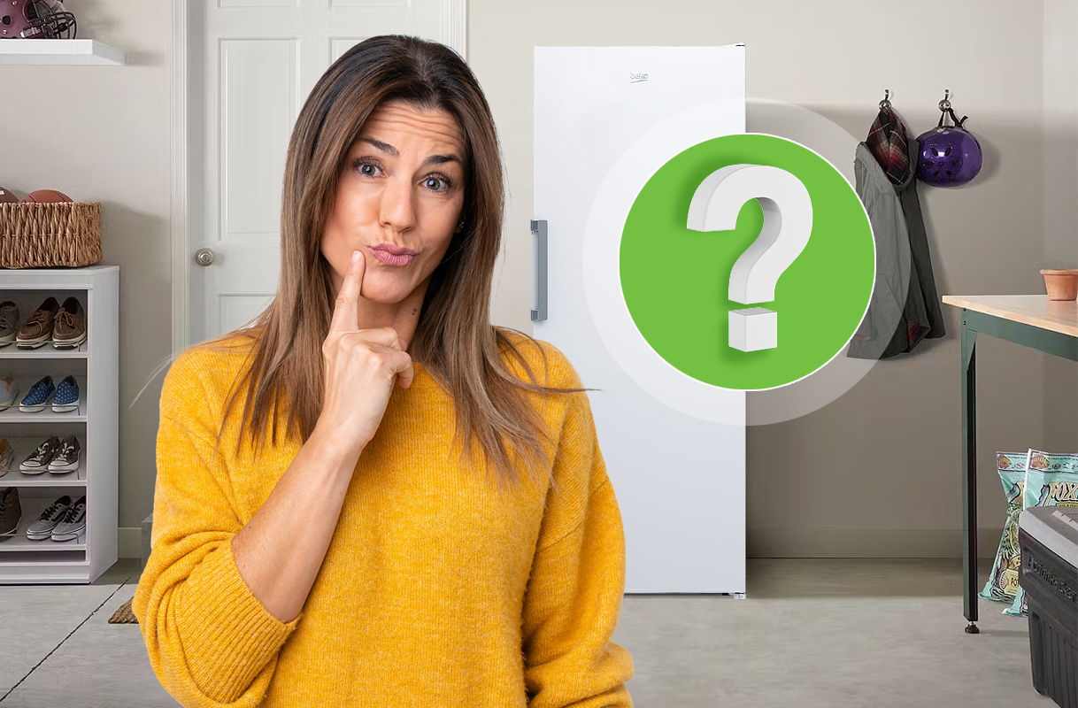 Vrouw die twijfelend naar een staande vriezer kijkt, symbool voor het moment waarop een oude of onzuinige vriezer vervangen moet worden.