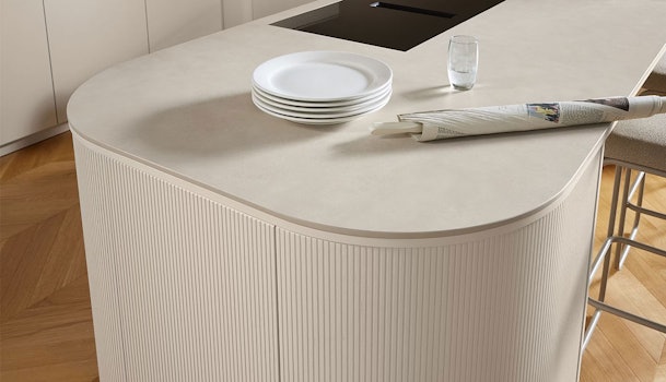Keukeneiland in beige zandkleur met afgeronde hoeken, keramiek werkblad en verticale ribbelstructuur voor een warme en serene uitstraling.
