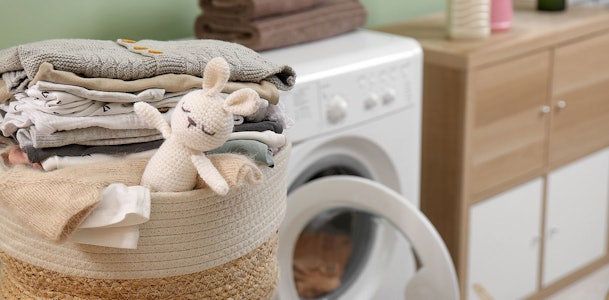 Wasmand met babykleding en knuffel naast wasmachine