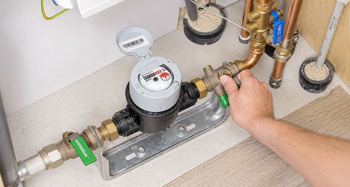 Hand draait de hoofdkraan naast de watermeter dicht om het water af te sluiten