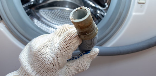 Hand met werkhandschoen houdt afvoerslang van wasmachine vast