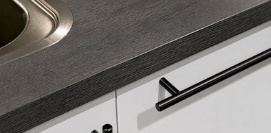 Detail van donker werkblad met houtstructuur, witte fronten en staafgreep met spoelbak